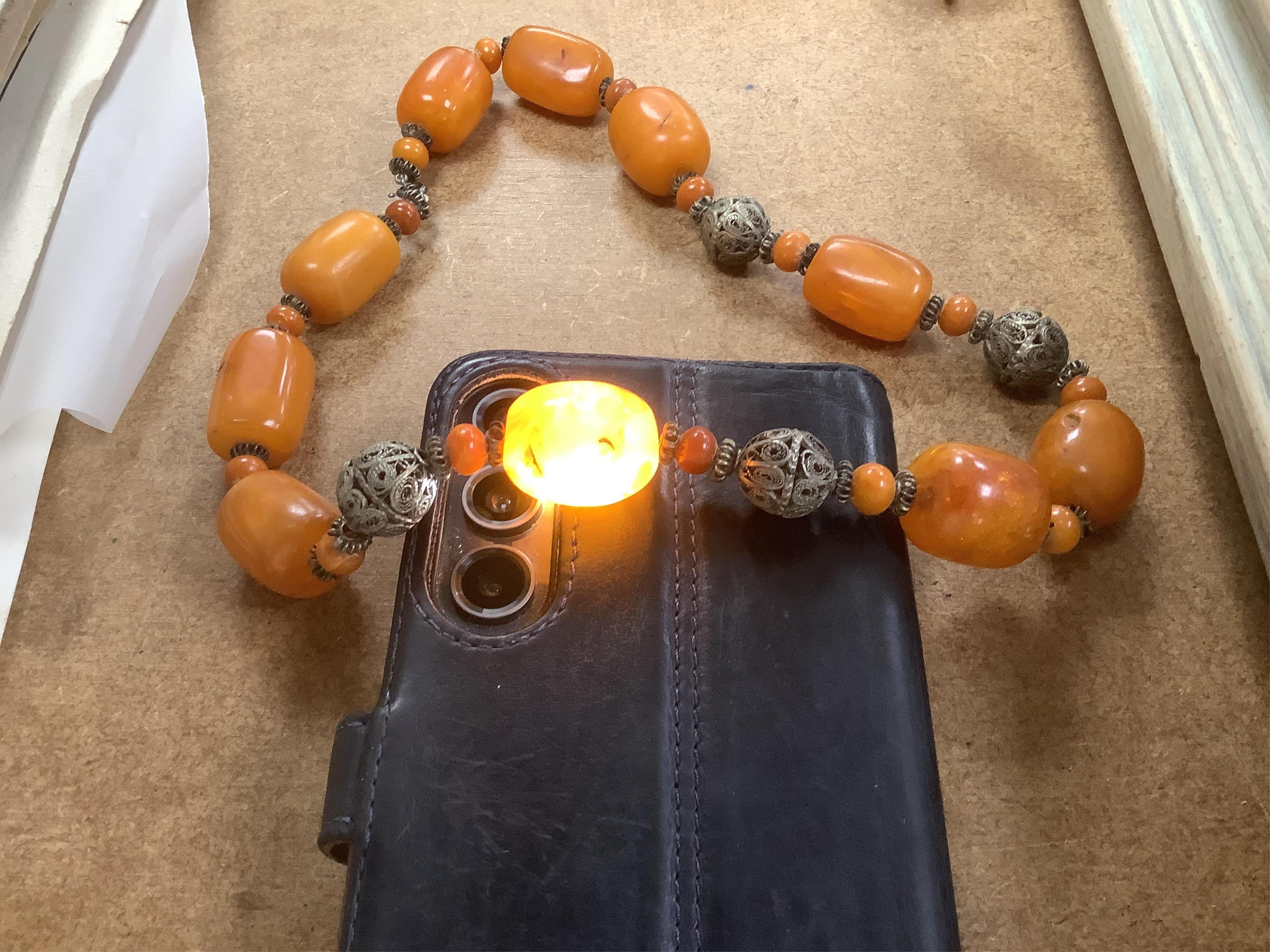 A single strand amber bead necklace, with filigree metal spacers, 48cm, gross 84 grams, together with a group of loose graduated simulated cherry amber beads, gross weight 117 grams.